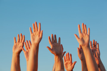 Ten raised up sunlit adult hands on the blue sky background