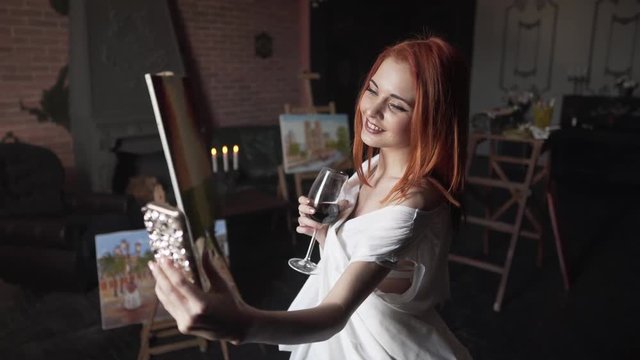 Beautiful redheaded girl taking photos of herself while holding a glass of wine