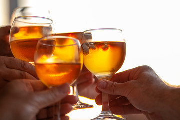 Four hands clinking four misted glasses with a drink, colored in gold by the background setting sun