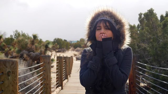 Attractive young woman shivering in freezing cold, stormy bad winter weather with rain drops under cloudy sky SLOW MOTION.