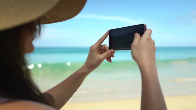 young traveler woman in hat taking photo on smartphone in ocean beach
