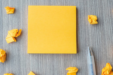 Empty yellow note paper with pen and crumbled paper on wooden table background. Blank copy space...