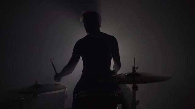 Silhouette of male drummer playing drums in dark