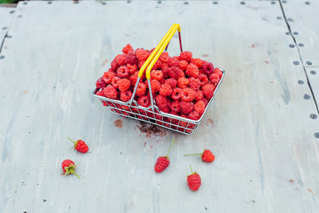 Mini shopping basket full of fresh red ripe raspberry on vintage background