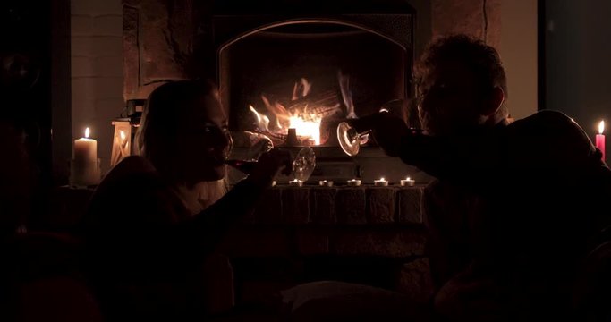 An attractive couple laying in front of a fireplace cheers with wine and candles
