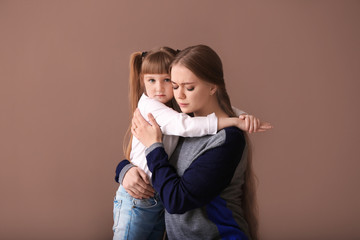 Sad woman after divorce hugging her little daughter on color background