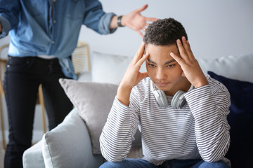 Sad African-American teenage boy having argument with his mother at home