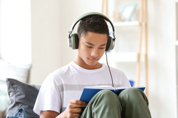 African-American teenage boy reading book at home