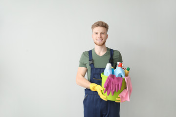 Portrait of male janitor with cleaning supplies on light background