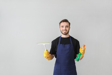 Portrait of male janitor with cleaning supplies on light background