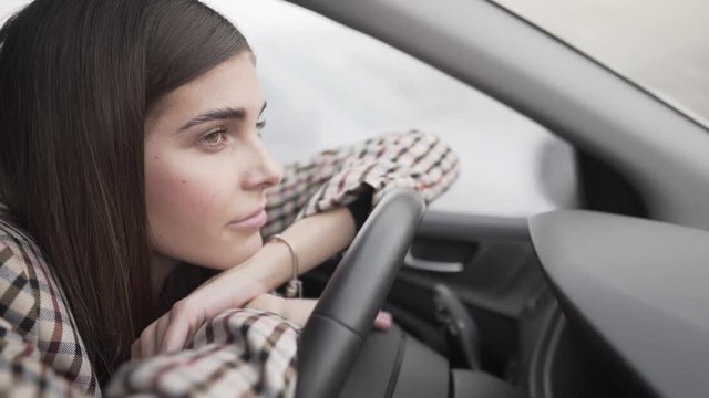 A lady leading on the steering wheel. The expression on her face  closeup view.