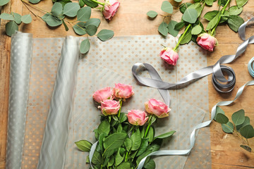 Beautiful flowers with ribbon and wrapping paper on wooden table