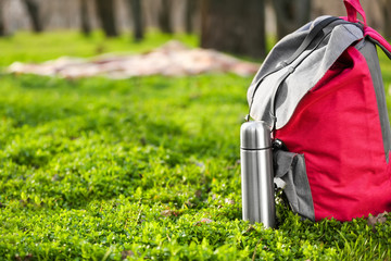 Thermos and backpack of tourist on meadow in forest