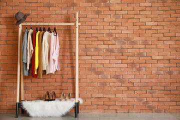 Rack with stylish clothes near brick wall