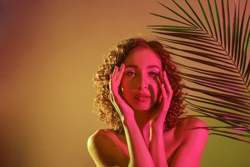 Toned portrait of beautiful young woman with tropical leaf on color background