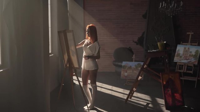 Naturally lit redhead woman painting on an easel in the studio