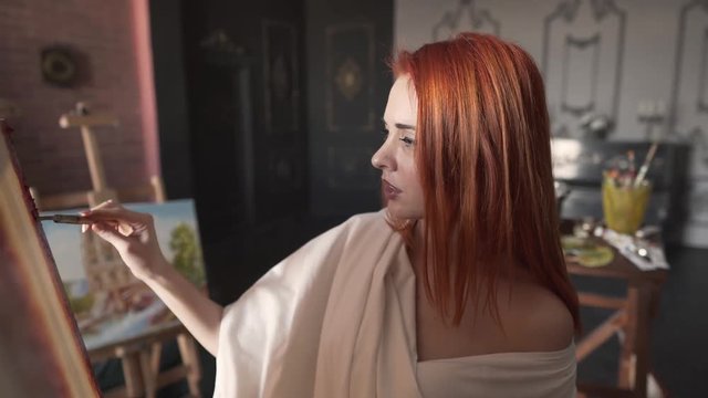 Beautiful woman applies paint to a canvas inside her art studio.