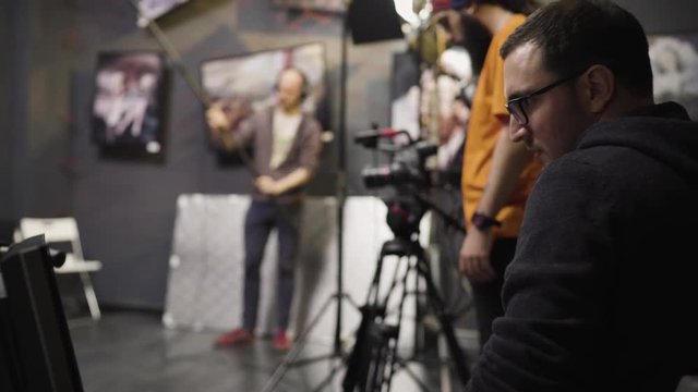 Male director with glasses is watching the monitor while directing a movie shooting