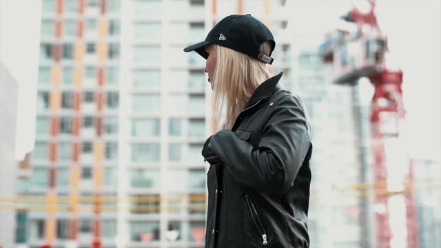 Cool looking attractive blonde women takes off her leather jacket and throws its at the camera whilst smiling, Shot in slow motion in a city scene.