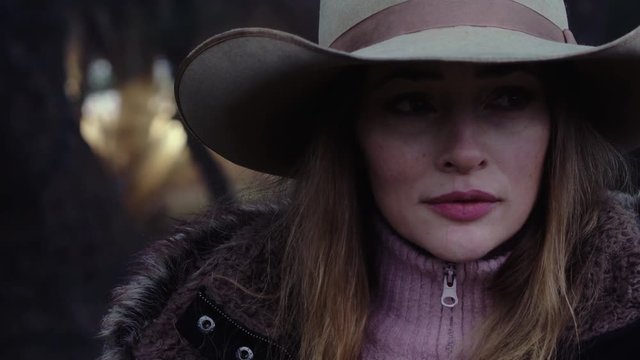 Close up of a woman wearing a cowboy hat, listening carefully for wildlife in the cold forest, slow motion 23.98 fps.
