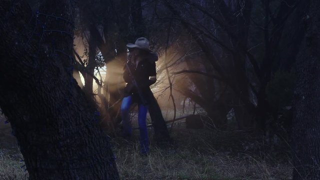 A cowgirl slowly enters the woods, holding a weapon & looking for wild animals to hunt, slow motion 23.98 fps.