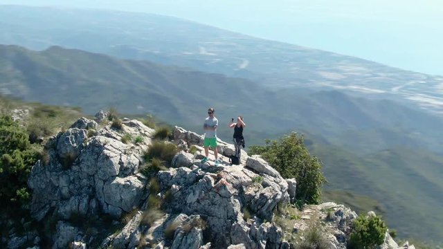Drone footage of woman taking photos with her cellphone and man enjoying the view from the mountains.
