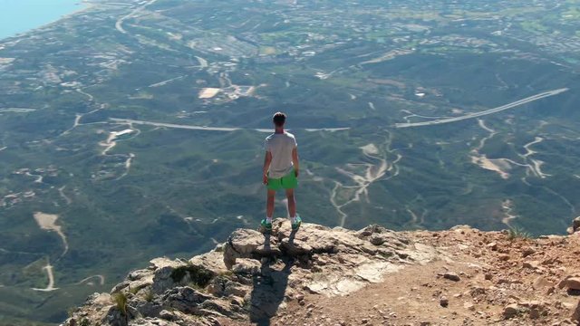 Drone circling and zooming in on male tourist while enjoying view towards Marbella from top of La Concha mountain. Group of friends in the background.