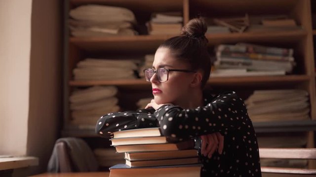 A hard-working female student is exhausted due to long cramming, so she has almost fallen sleep on the pile of books in the library. At some point, she wakes up and looks into the window tiredly.