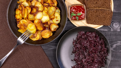 Fried potato chips in a pot with dark rye bread on a wooden plate and homemade stewed cabbage, on a black rustic background