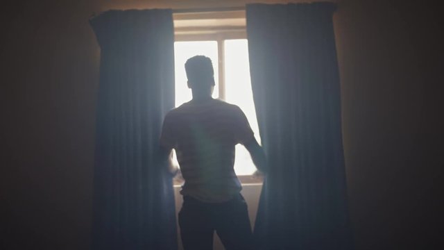 African American man opening the curtains in a dark room in the morning