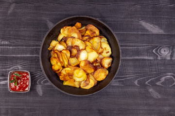 Fried homemade potato chips in a vintage old cast iron pan and tomato ketchup on a wooden rustic background