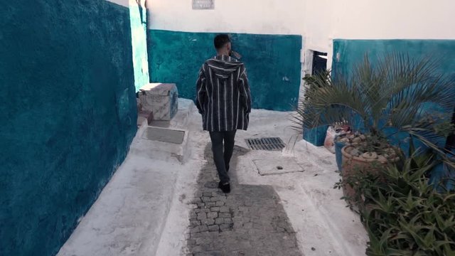 A tourist man exploring streets i Chefchaouen city of Morocco, and wearing the official swearter in Chafchaouen, walking between blue and withe houses.