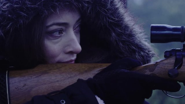 Close up side profile of a woman holding still while aiming a rifle at night, 23.98 fps.