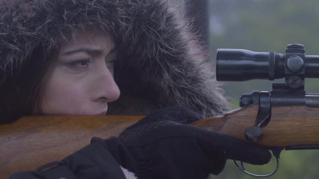 Close up side profile of a woman holding still while aiming a rifle, 23.98 fps.