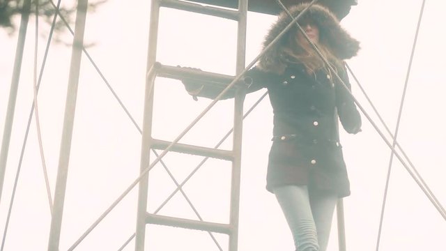 A woman climbs to the top of a metal outpost structure on a rainy day, 23.98 fps.