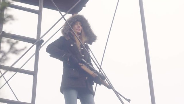 An woman stands guard on top of a metal outpost tower, holding a rifle, 23.98 fps.