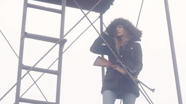 An woman holding a weapon watches on top of a metal tower fort protecting the area, 23.98 fps.