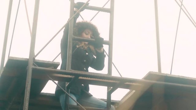 A woman climbing to the top of a metal outpost structure on a cold day, 23.98 fps.