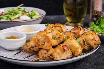 Grilled chicken kebab and salad with cucumber, radish, onion on a dark background.