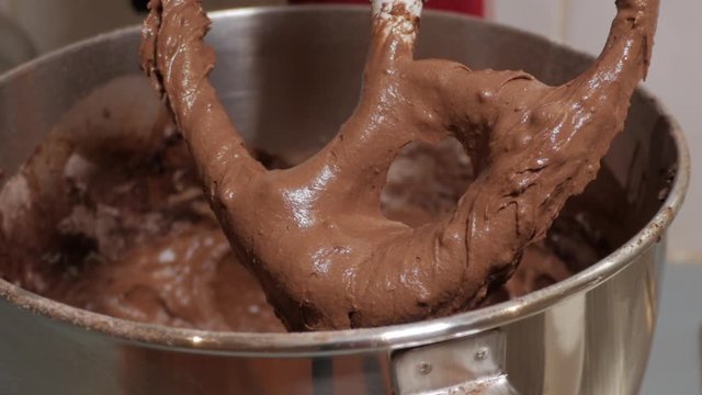Male preparing a chocolate cake. Mixture drips of the spatular into the bowl after contents has been mixed together. ZOOM IN SHOT.