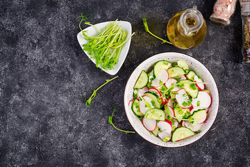Fresh vegetable  radish and cucumber salad with green onions and microgreens peas on a dark background. Healthy food. Top view. Copy space.
