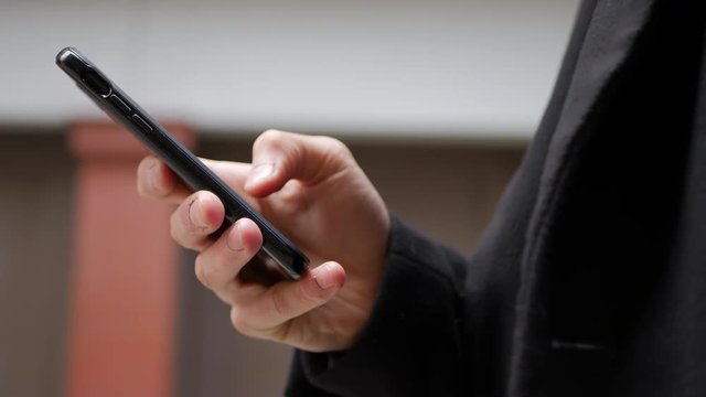 Hand scrolling on a black smartphone with a protective case