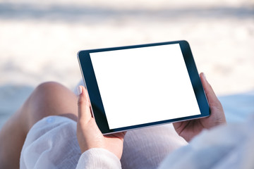 Mockup image of a woman holding a black tablet pc with blank desktop screen while laying down on...