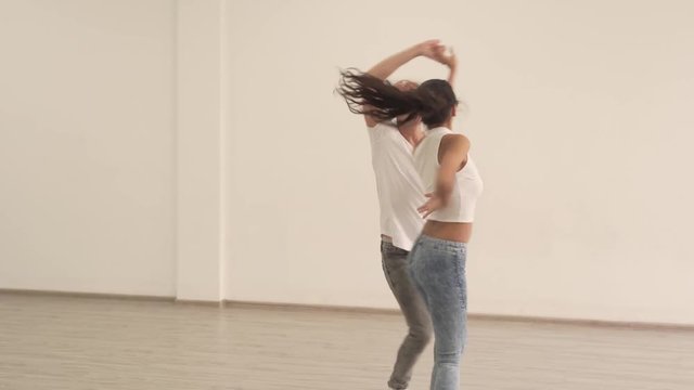 Young Female Dancer in Jeans White Shirt High Heels Shoes and Hair in Pigtain Spinning in Front of Her Male Dance in Dance Studio Partner While He Holds Her Hands