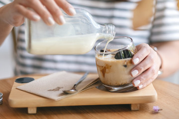 Closeup image of a woman pouring milk into a glass of ice cube coffee in cafe