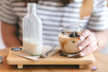 A woman holding a glass of iced coffee and a bottle of milk on wooden saucer