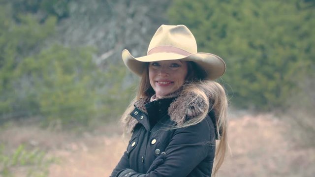 A female rancher with long hair looks happy, standing outdoors on the farm.