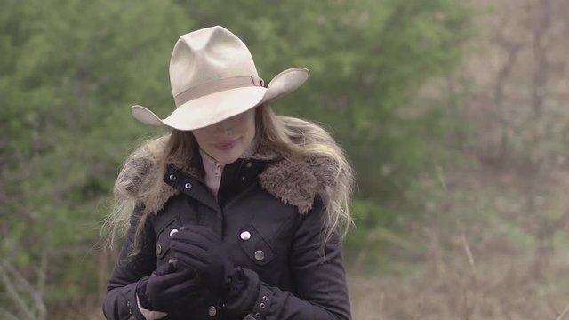 A cowgirl adjusts her gloves during winter out on the farm.