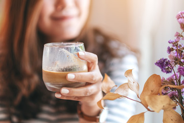 Closeup image of a beautiful woman holding a glass of iced coffee to drink in cafe