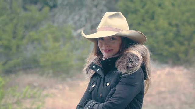 A happy and flirtatious woman wearing a cowboy hat and rugged up for winter, 29.97 fps.